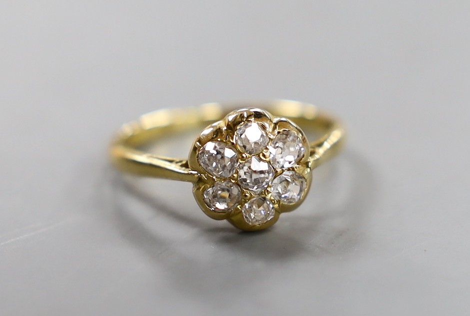 An 18ct and seven stone diamond set circular cluster ring, size M/N, gross weight 2.7 grams.